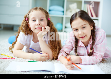 Zwei kleine Mädchen Blick in die Kamera, während Sie auf dem Boden liegend und Zeichnung Stockfoto