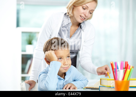 Porträt von müde Junge sitzt vom Schreibtisch beim Tutor erklären, etwas in der Nähe von Stockfoto