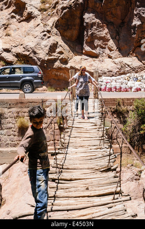 Eine weibliche touristische Kreuze über eine möglicherweise gefährliche Rickety Bridge über den Fluss Ourika, Ourika Valley, Atlas, Marokko Stockfoto