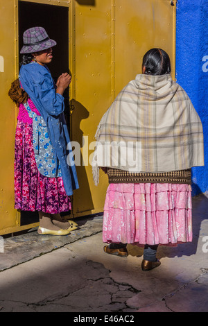 Zwei Nachbarn Frauen, gekleidet in traditioneller Kleidung sprechen außerhalb des Hauses eine davon in Copacabana, Bolivien. Stockfoto