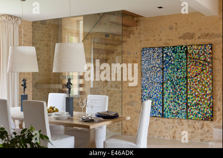 Esszimmer mit abstrakter Malerei an der Wand und Esstisch mit zwei Lampenschirmen Stockfoto