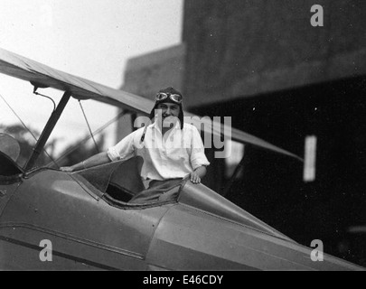 Dieses Bild zeigt eine junge Frau in einem Cockpit, lächelnd und trägt eine Schutzbrille und einen Helm, eine Darstellung der frühen weiblichen Beteiligung in der Luftfahrt. Stockfoto