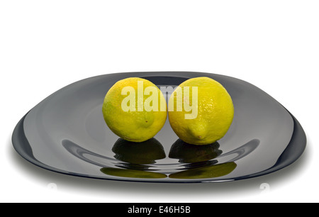 Zwei frische Zitronen auf einer schwarzen Platte isoliert auf weißem Hintergrund Stockfoto