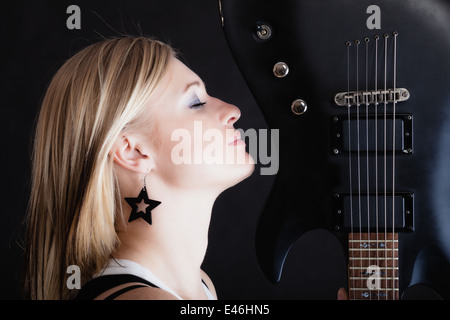 Rock-Musik. Blonde Mädchen Gitarrist Musiker-Performer mit e-Gitarre musikalische Saiteninstrument auf schwarz. Konzert. Stockfoto