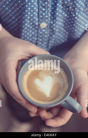 Hände halten eine graue Tasse mit Liebe Herzform in der crema Stockfoto