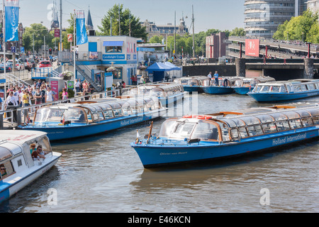 Amsterdam Central Station Cruise Boote Schlange, um Touristen auf eine Rundfahrt durch die berühmten Grachten die Grachtengordel nehmen. Stockfoto