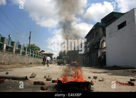 Srinagar, Kaschmir. 4. Juli 2014. Kaschmirische Muslime gehen vorbei an brennenden Reifen während eines spontanen Streiks im indischen Kaschmir Srinagar am Juli 4.2014. separatistische Gruppen gegen indischen Herrschaft kündigte einen Streik um einen Besuch des Landes Premierminister Narendra Modi zu protestieren. Modi ist auf seinem ersten offiziellen Besuch in der umstrittenen Himalaya Region ...er zu eröffnen, eine Eisenbahnlinie und ein Kraftwerk und auch Kredit-Überprüfung Sicherheit und Entwicklung: Shafat/Pacific Press/Alamy Live News Stockfoto