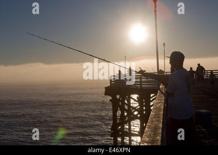 Mann Angeln auf Crystal Pier, eine öffentliche Pier und Hotel, im Februar 2014. Am späten Nachmittag ist die Sonne eine Nebelbank aufschlussreich. Stockfoto