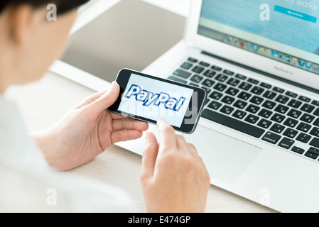 Person am Arbeitsplatz halten in der hand eine brandneue Apple iPhone 5 s mit PayPal-Logo auf einem Bildschirm Stockfoto