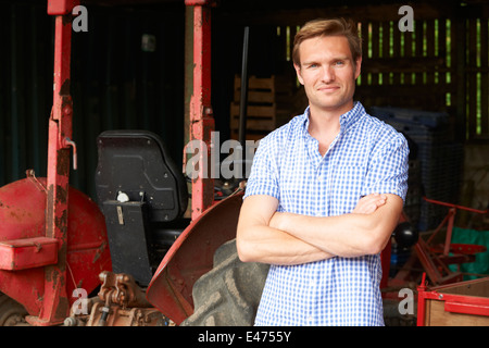 Landwirt stehen neben alten altmodisch Traktor In der Scheune Stockfoto