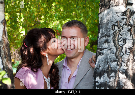 Kaukasische Frau ist küssen ihren lächelnden Mann in der Nähe von der Birke Stockfoto