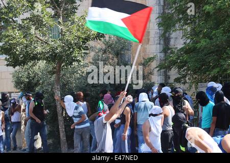 Shufat, annektierte Ost-Jerusalem, Israel. 4. Juli 2014. Eine palästinensische Jugend hält einen Stein in der Hand und ein Flag in der anderen, nachdrücklichen Aufforderung an alle Männer, aufzustehen und zu widerstehen. Im Anschluss an die Beerdigung von Muhammed Abu Khdeir Zusammenstöße brach fast sofort nach. Palästinensische Jugendliche aus dem Dorf schleuderten Felsen auf die israelischen Streitkräfte. Spannungen haben wochenlang nun seit der Tötung von drei israelischen Jugendlichen und jetzt dieses scheinbare Rache töten eskaliert. Bildnachweis: Anna Ferensowicz/Pacific Press/Alamy Live-Nachrichten Stockfoto