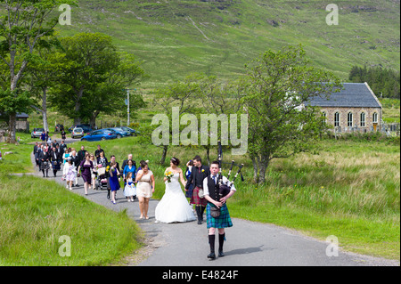 Highland schottische Hochzeit.  Pfeifer führt die Prozession der Braut, Bräutigam und Gäste von hebt Kirche in den Highlands von Schottland Stockfoto