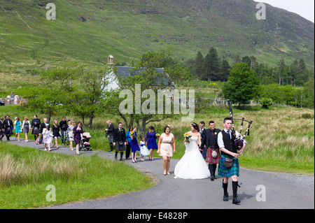 Highland schottische Hochzeit.  Pfeifer führt die Prozession der Braut, Bräutigam und Gäste von hebt Kirche in den Highlands von Schottland Stockfoto