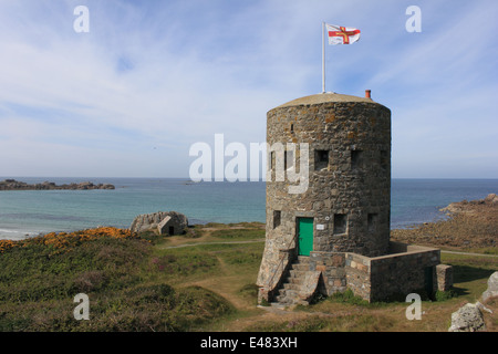 Ein Schlupfloch-Turm auf der Küste von Guernsey mit das Guernsey Flagge hissen Stockfoto