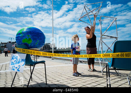 Aberystwyth, Wales, UK. 5. Juli 2014.  Freunde von der Erde Cymru, Mitte und West Wales Anti-Fracking Gruppe organisiert einen Tag voller Veranstaltungen und Aktivitäten an dort Promenade in Aberystwyth zur Sensibilisierung für die Gefahren des Trackings für Gas in Wales.  Der Gelenk-Organisatoren NICKI SINDALL und ihr Sohn OZ den letzten Schliff auf einer Bohrinsel, umgeben von Polizei Kriminalität Szene Band Photo Credit: Keith Morris/Alamy Live-Nachrichten Stockfoto