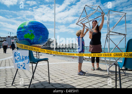 Aberystwyth, Wales, UK. 5. Juli 2014.  Freunde der Erde-Cymru, mit der Mitte und West Wales Anti-Fracking Gruppe organisierte einen Tag von Veranstaltungen und Aktivitäten an der Promenade in Aberystwyth zur Sensibilisierung für die Gefahren des Trackings für Gas in Wales.  Der Gelenk-Organisatoren NICKI SINDALL und ihr Sohn OZ den letzten Schliff auf einer Bohrinsel, umgeben von Polizei Kriminalität Szene Band Photo Credit: Keith Morris/Alamy Live-Nachrichten Stockfoto