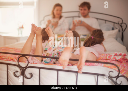 Mädchen (4-5, 6 und 7) liegen im Bett der Eltern, während Mutter und Vater Frühstück Essen Stockfoto