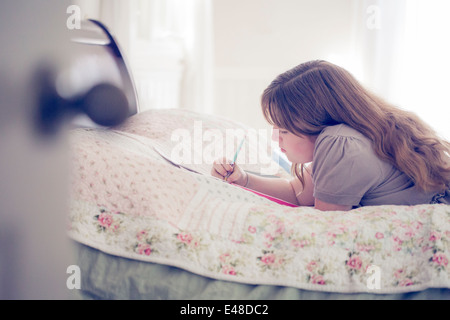 Teenager-Mädchen (13-15) im Bett liegen und schreiben Stockfoto