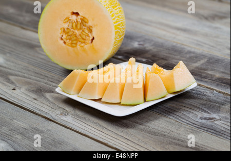 Detailansicht einer frisch geschnittenen Melone mit Scheiben auf weißen Teller und die Hälfte der Melone im Hintergrund auf rustikalen Holz Stockfoto