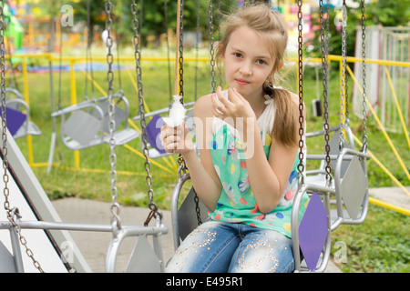 Hübsches kleines Mädchen Zuckerwatte Garaus den letzten Bissen zu essen, als sie auf einer Schaukel in einem Vergnügungspark oder Spielplatz sitzt Stockfoto