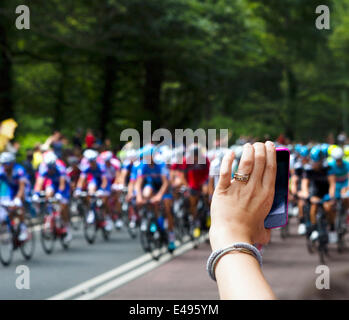 Frau, die ein Foto mit einem Smartphone das Hauptfeld nähert sich Holmfirth am 2. Etappe der Tour de France 2014. Tausende von Menschen die Straßen gesäumt von vielen drängeln, um Fotos der schnellere Fahrer zu machen. West Yorkshire, Großbritannien Stockfoto