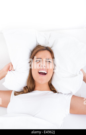 Bild der irritiert und schreien junge lässige Frau auf Bett liegend und schließen ihre Ohren mit Kissen. Lärm oder Schlaflosigkeit-Konzept Stockfoto