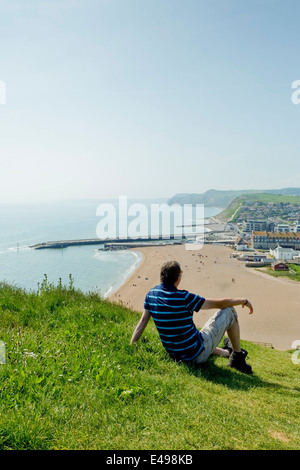 Mann sitzt auf der Klippe mit Blick auf West Bay, Dorset, England, UK Stockfoto