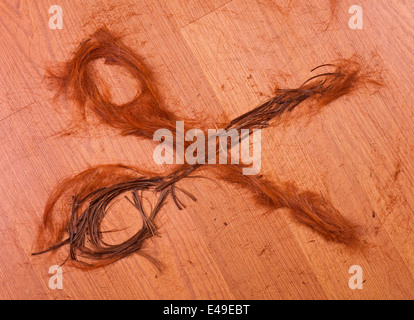 Haar in Form von Scheren auf hölzernen Hintergrund abgeschnitten Stockfoto