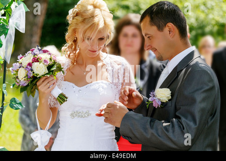 schönes junges Paar in der Hochzeit Zeremonie im Freien, blonde Braut mit Blume und Bräutigam Austausch von Trauringen Stockfoto