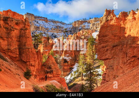 Wanderer nimmt sich eine Auszeit auf der Peekaboo Loop Trail im Winter mit verschneiten roten Felsen und Klippen, Bryce-Canyon-Nationalpark, Utah, USA Stockfoto