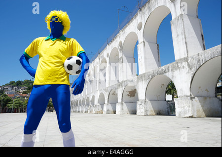 Blauer brasilianischer Fußballspieler im gelben Hemd halten Fußball Ball stehend in Lapa Bögen Rio de Janeiro Brasilien Stockfoto