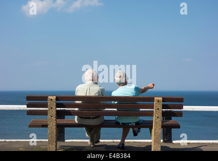 Älteres Ehepaar sitzt auf der Bank mit Blick auf Meer. UK Stockfoto