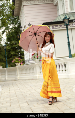 Thai Mädchen kleiden und Regenschirm mit traditionellen Stil (Palast im Hintergrund) Stockfoto