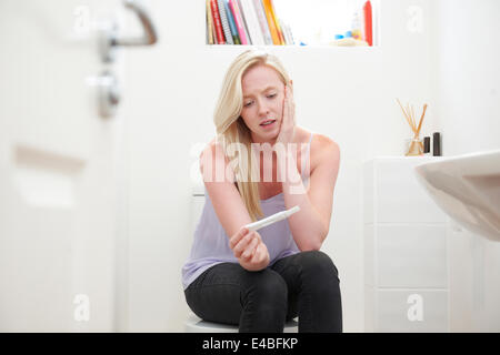 Teenager-Mädchen sitzen im Badezimmer mit Schwangerschaftstest besorgt Stockfoto