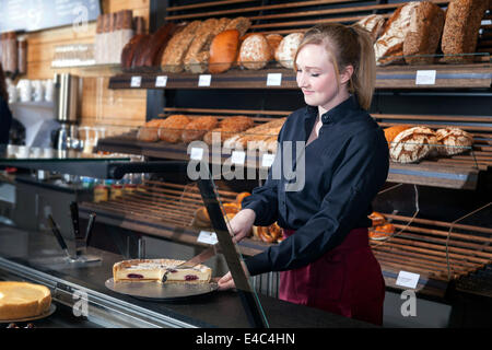 Weibliche Verkäuferin schneiden einen Kuchen am Schalter Stockfoto