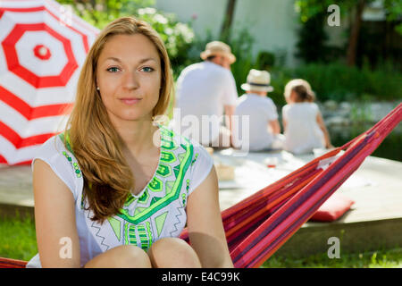 Frau sitzt auf der Hängematte, Familie im Hintergrund, München, Bayern, Deutschland Stockfoto