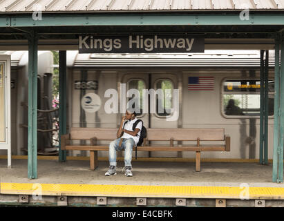 Junger Mann steckte in seinem Smartphone wartet auf eine u-Bahn Haltestelle Kings Highway auf der B-Linie in Brooklyn, New York. Stockfoto