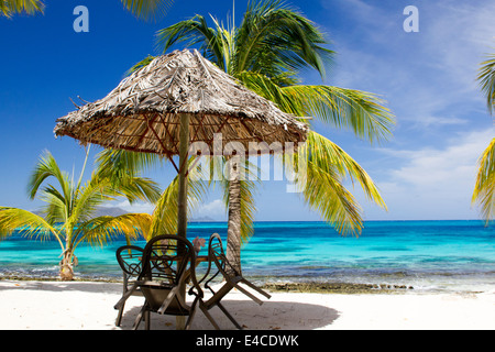 Romantischer Strand Beistelltisch unter einem Palm Frond Sonnenschirm mit einer atemberaubenden karibischen Aussicht. Stockfoto