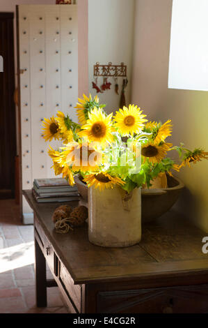 Krug mit Sonnenblumen auf alten Holztisch Konsole in Eingangshalle mit Nieten Tür und geflieste Terrakottaboden Stockfoto