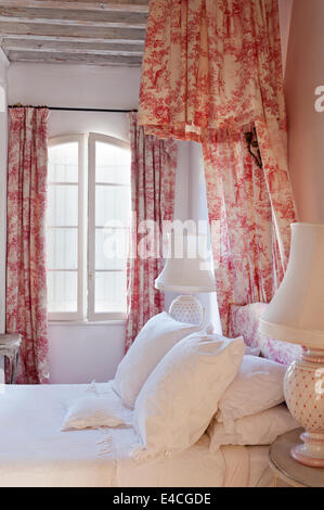 Rosa und weiße Toile De Jouy Stoff Vorhänge und Coronet Betthimmel in Schlafzimmer mit Holzbalken und Nachttischlampen Stockfoto