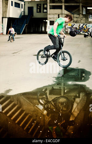 BMX-Biker bei einem Stunt über eine Pfütze Mann im Hintergrund Stockfoto