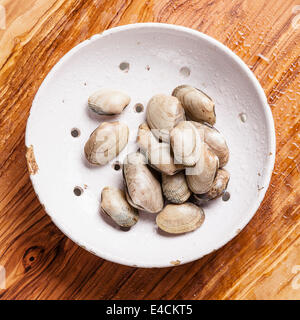 Roher Muscheln Vongole in Vintage Keramik Sieb auf Oliven Holz Hintergrund Stockfoto