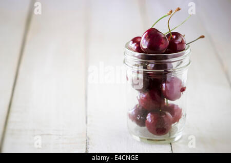 Kirschen in einem Glas auf eine hölzerne Tafel. Stockfoto