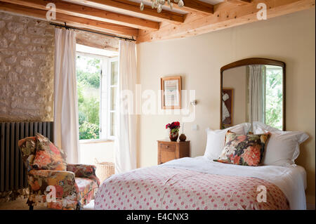 Antike Persische bestickte Quilt auf Bett im Schlafzimmer mit Steinmauern und Holzbalken. Der Sessel ist in fl gepolstert. Stockfoto