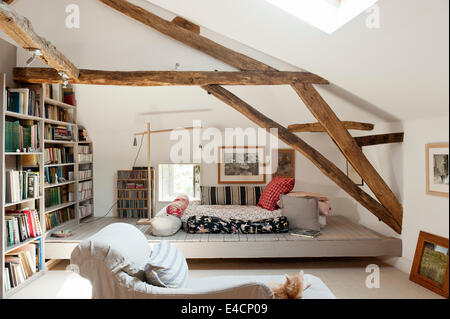 Dachzimmer mit Holzbalken, große Büchergestell, Bodenkissen und Chaiselongue Stockfoto