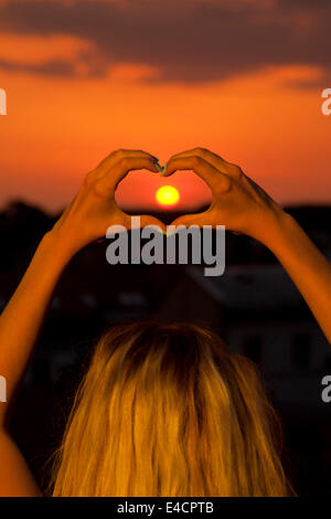 Junge Frau macht eine Herzform gegen Sonnenuntergang, Osijek, Kroatien Stockfoto