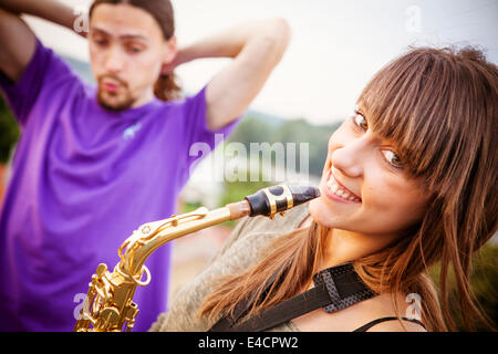 Junge Frau mit Saxophon, Freund im Hintergrund Stockfoto