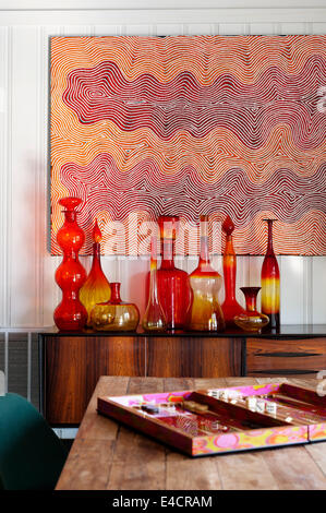 Eine Sammlung von amerikanischen Blenko Glas steht auf einer 50er Jahre Palisander Anrichte. Das Gemälde an der Wand ist von einer australischen Aborigi Stockfoto