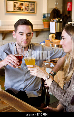 Junges Paar Toasten mit Bier in der Kneipe, Dorset, Bournemouth, England Stockfoto